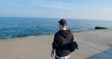 junger Mann mit Skateboard, der sich in der Nähe des Meeres entspannt foto