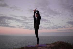 fitte Frau, die Yoga-Stretching-Übungen im Freien in einer wunderschönen Berglandschaft macht. frau auf dem felsen mit meer und sonnenaufgang oder sonnenuntergang hintergrund training asans. Silhouette der Frau in Yoga-Posen foto