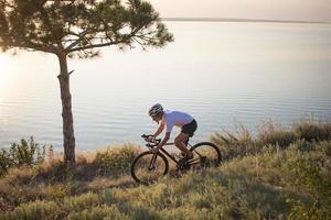 Fahrradfahrer auf professionellem Cyclocross-Rad fahren bergab, Kiefern- und Seehintergrund foto