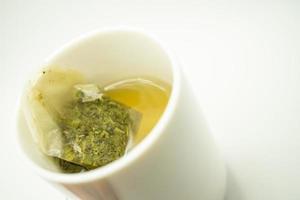 Grünteebeutel in einer Tasse. Tasse aromatischen grünen Tee auf weißem Hintergrund. Tasse mit grünem Tee in isoliert. foto