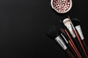 Make-up-Pinsel und Kosmetik auf schwarzem, isoliertem Hintergrund. Draufsicht und Attrappe foto