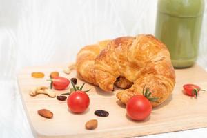 Croissant mit roten Tomaten isoliert auf Holzplatte, frisch gebackenes Brot für ein einfaches Frühstück. foto