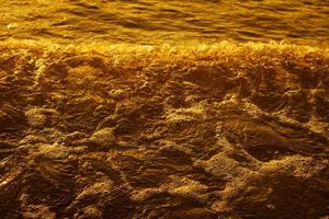 goldenes licht, das bei sonnenuntergang von einer wasserwelle am meer und sand reflektiert wird. reiner Goldton foto