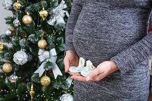 junge schwangere frau mit geschwollenem bauch und babysocken in der hand, die gegen den weihnachtsbaum posiert foto