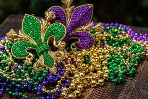 Mardi Gras Farbperlen mit Fleur de Lis auf Holztisch im Sonnenlicht foto