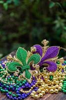 Mardi Gras Farbperlen mit Fleur de Lis auf Holztisch im Sonnenlicht foto