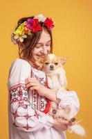 Teenager-Mädchen mit einem Kranz auf dem Kopf und einem bestickten Hemd mit einem Chihuahua-Hund. Haustier. foto