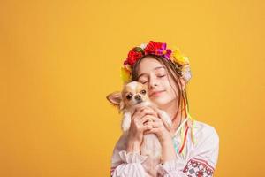 Teenager-Mädchen mit einem Kranz auf dem Kopf und einem bestickten Hemd mit einem weißen Chihuahua-Hund. foto