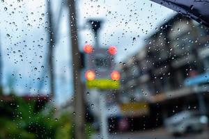 Regentropfen auf der Oberfläche des Autoglases mit verschwommenem Verkehrszeichenhintergrund durch das Fensterglas des Autos, das von Regentropfen bedeckt ist. Nasse Windschutzscheibe aus dem Auto heraus geschossen. foto