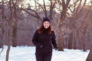 Junge Sportlerin im schwarzen Sportanzug läuft im Winterpark foto