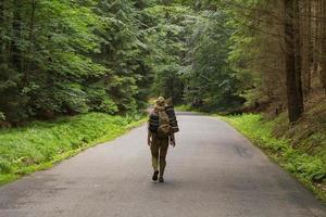 junge Wandererin, die auf einer schmalen Straße durch den sommergrünen Wald geht foto