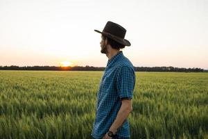 Junger männlicher Bauer steht während des Sonnenuntergangs allein im Weizenfeld foto