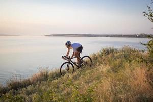 Fahrradfahrer auf professionellem Cyclocross-Rad fahren bergab, Kiefern- und Seehintergrund foto