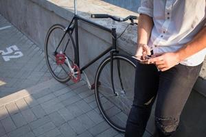 junger bärtiger mann mit lederrucksack, der mit schwarzem fahrrad geht foto