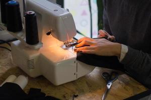 Näherin bei der Arbeit auf dem Tisch, Schneiderfrau arbeitet im Studio mit Kleidung foto