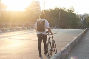 junger bärtiger mann mit lederrucksack, der mit schwarzem fahrrad geht foto