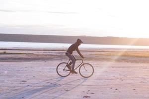 Alleinfahrer auf Rennrad mit festem Gang in der Wüste in der Nähe des Flusses, Bilder von Hipster-Touristenradfahrern. foto