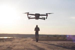 bild von schwarz schindendem quadrocopter dron und pilot siluette im sonnenuntergang hellen hintergrund, touristen nutzen dron hubschrauber zum fotografieren oder filmen von wüstenlandschaften foto