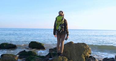 junge weibliche reisende mit rucksack und retro-filmkamera reisen in den herbstbergen nahe meer foto