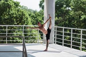 junger Mann mit Tätowierungen macht Yoga-Übungen im Freien auf dem Balkon foto