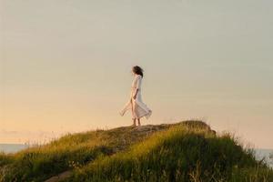 junge frau, die in einem schönen weißen kleid am morgenstrand spazieren geht. fitte frau, die sich während des aufgangs des sonnenaufgangs gut amüsiert. foto