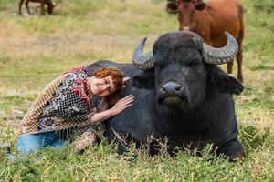 Junge Frau in einem Poncho reitet auf einem großen Wasserbüffel foto