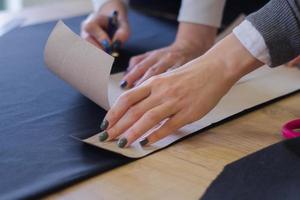 Näherin bei der Arbeit auf dem Tisch, Schneiderfrau arbeitet im Studio mit Kleidung foto