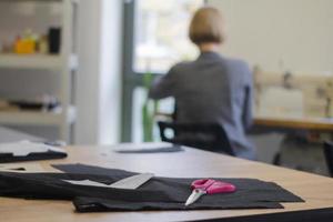 Näherin bei der Arbeit auf dem Tisch, Schneiderfrau arbeitet im Studio mit Kleidung foto