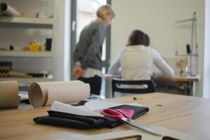 Näherin bei der Arbeit auf dem Tisch, Schneiderfrau arbeitet im Studio mit Kleidung foto