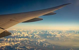 flügel des flugzeugs über bergdecke mit weißem schnee. Flugzeug fliegt am blauen Himmel. malerische Aussicht aus dem Flugzeugfenster. Flug einer kommerziellen Fluggesellschaft. Flugzeugflügel. Konzept der Flugmechanik. internationaler Flug. foto