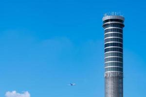 Flugsicherungsturm auf dem Flughafen mit internationalem Flugflugzeug, das am klaren blauen Himmel fliegt. Verkehrskontrollturm für Flughäfen zur Kontrolle des Luftraums durch Radar. Luftfahrttechnik. Flugmanagement. foto