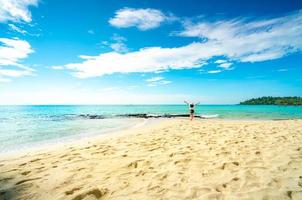 glückliche junge frau in weißen hemden und shorts, die am sandstrand spazieren gehen. entspannen und urlaub am tropischen paradiesstrand mit blauem himmel und wolken genießen. Mädchen in den Sommerferien. sommergefühl. glücklicher Tag. foto