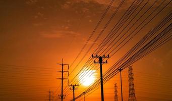 Hochspannungsmast und Übertragungsleitungen bei Sonnenuntergang mit orangefarbenem und rotem Himmel und Wolken. die Architektur. Silhouette Strommasten während des Sonnenuntergangs. Kraft und Energie. Energieeinsparung.
