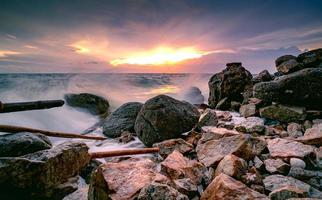 meerwasserspritzer am felsstrand mit schönem sonnenunterganghimmel und wolken. meereswelle, die im sommer auf stein am meer spritzt. Naturlandschaft. tropischer Paradiesstrand bei Sonnenuntergang. Felsenstrand an der Küste. foto