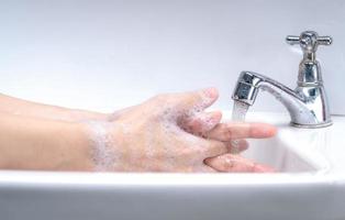 Frau wäscht sich die Hand mit Seifenschaum und Leitungswasser im Badezimmer. handreinigung unter wasserhahn am waschbecken für die persönliche hygiene zur vorbeugung von grippe und coronavirus. gutes Verfahren der Handwäsche, um Bakterien und Viren abzutöten. foto