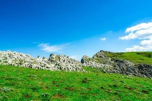 Landschaft aus grünem Gras und Felshügel im Frühjahr mit schönem blauem Himmel und weißen Wolken. Landschaft oder ländliche Aussicht. Naturhintergrund am sonnigen Tag. foto