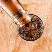 Gießen von Cola in das Glas auf Holztisch, Draufsicht. foto