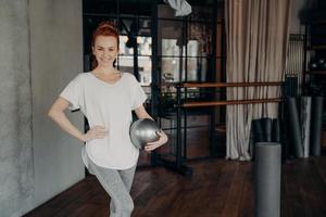 lächelnde fitte frau, die mit pilatesball im fitnessstudio aufwirft foto