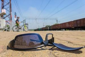 die zerbrochene brille liegt am bahnhof vor dem hintergrund der vorbeifahrt des jungen mit dem fahrrad und dem fahrenden zug foto