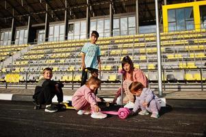 junge stilvolle mutter mit vier kindern im freien. Sportfamilie verbringt ihre Freizeit im Freien mit Rollern und Schlittschuhen. mit Kreide auf den Asphalt gemalt. foto