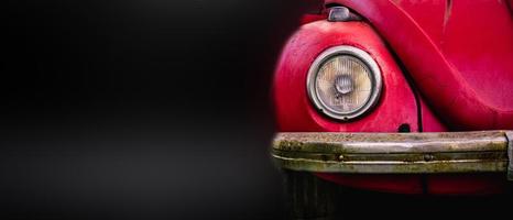 Vorderansicht des alten roten Autos des Detailscheinwerfers im dunklen Garagenhintergrund. foto
