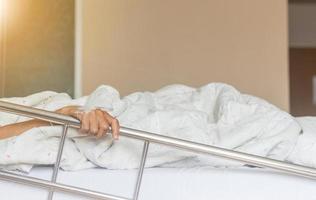 Nahaufnahme der Hand des asiatischen älteren Frauenpatienten auf einem Tropf, der eine Kochsalzlösung erhält, die sich am Bett im Krankenhaus festhält foto