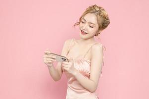 Porträt fröhliche hübsche junge Asiatin aufgeregt mit Smartphone in der Hand auf rosa Hintergrund. tolles mobiles angebot, konsum, lifestyle-konzept. foto