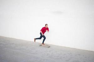 junger bärtiger mann, der auf skateboard, hipster mit longboard in rotem hemd und blauem jeans-stadthintergrund fährt foto