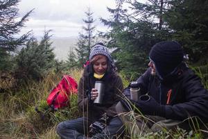 junges paar wanderer mit thermobechern im wald, reisende in den bergen, die tee oder kaffee trinken