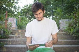 junger Student, der ein Gadget für das Internet verwendet oder im Park liest foto