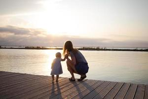 mutter und tochter, die am sonnigen tag auf dem holzsteg spazieren, glückliche familie am strand foto