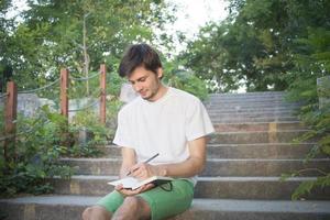 junger mann outddur im park schreibt in notizbuch, student oder schriftsteller bei der arbeit foto