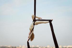 Übungen mit Luftseide im Freien, Himmelshintergrund. schöne fitte frau, die akrobatik in der luft trainiert. foto