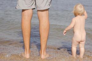 Nahaufnahme des Vaters mit einem einjährigen Kind, das im Sommer am Strand spazieren geht foto